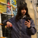 Man outside in urban environment with graffiti backdrop, casually looking at phone. 